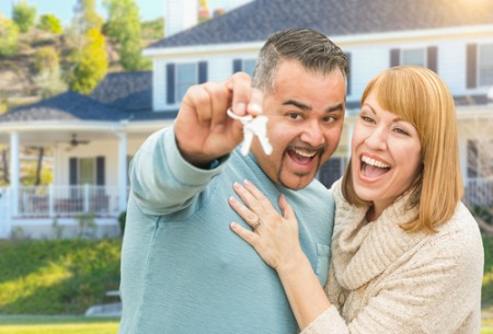 man and woman smiling and embracing while man holds house keys